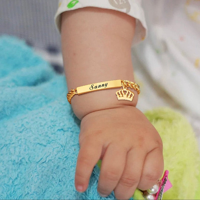 Newborn baby wearing a Personalized custom baby bracelet in 14k yellow gold plated stainless steel for reborn dolls and newborn baby girls with a crown charm.