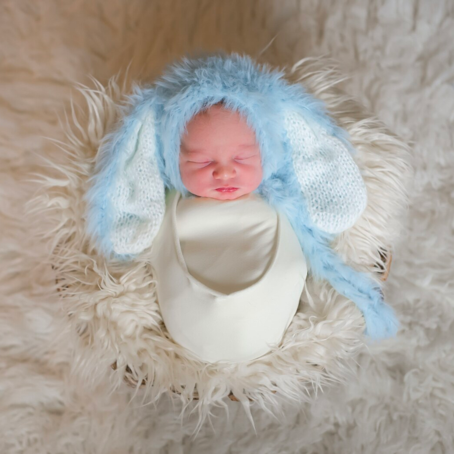 Newborn baby photoshoot where baby boy is wearing the blue floppy eared fuzzy knitted mohair baby bunny bonnet for newborn photography and baby dolls.