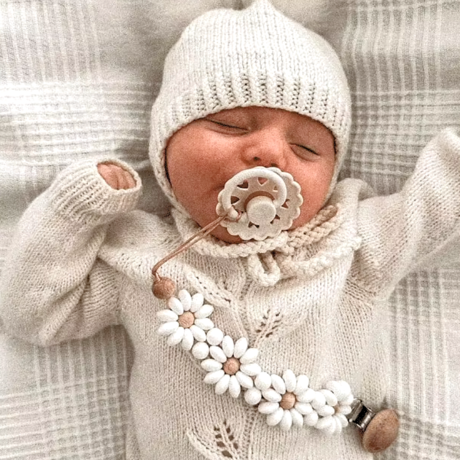 Newborn baby wearing a white Boho baby pacifier clip in the shape of a daisy flower. Made of silicone saucer beads on a wooden clip with wooden beads for reborn dolls.