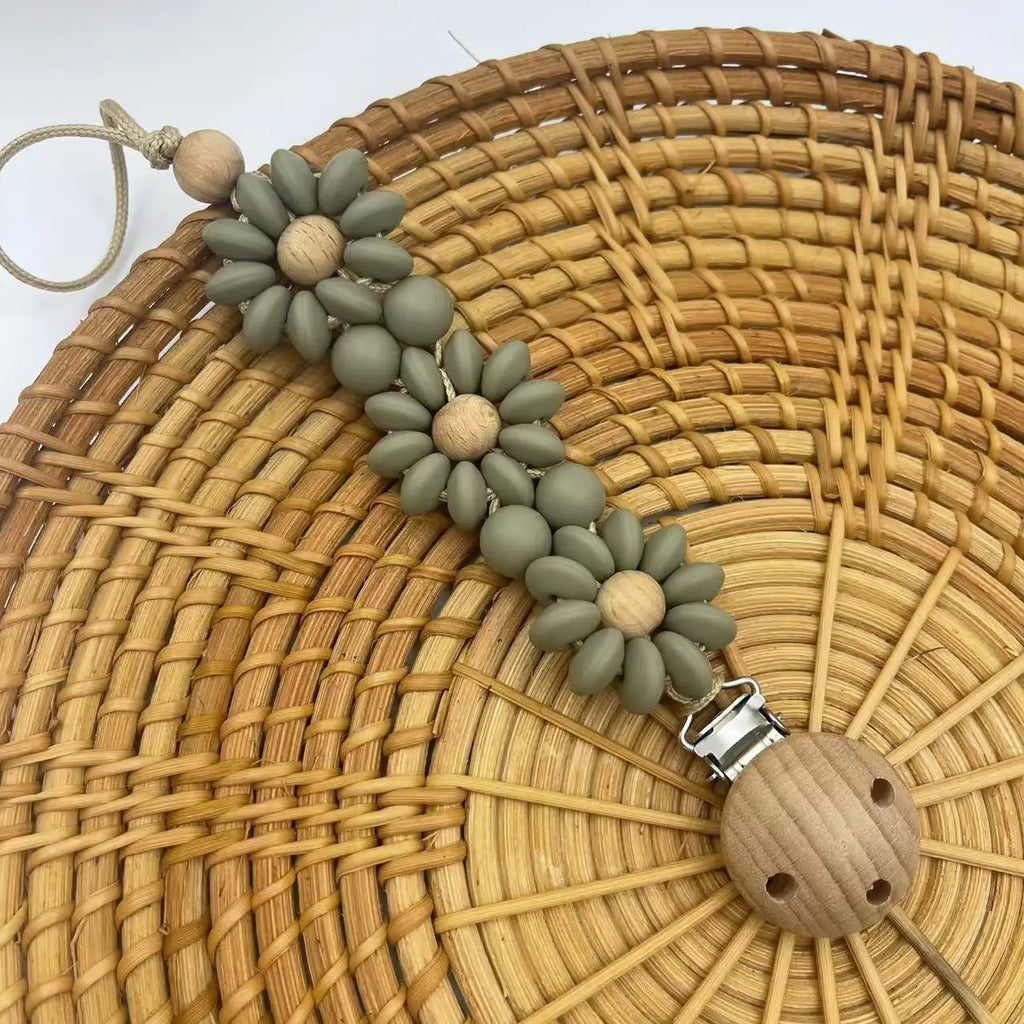 Sage green Boho baby pacifier clip in the shape of a daisy flower. Made of silicone saucer beads on a wooden clip with wooden beads for reborn dolls.