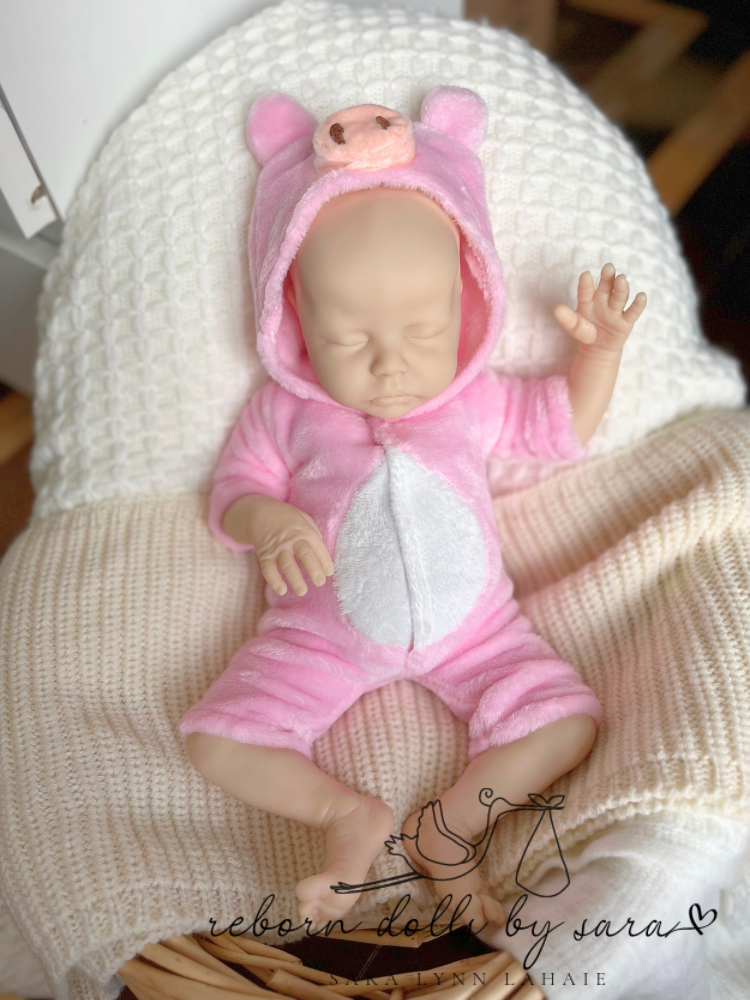 Delilah by Nikki Johnston wearing a preemie sized romper for reborn dolls.  Reborn doll clothing pig romper.  