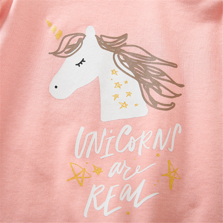 Close-up of the unicorn face with stars on it from a pink long-sleeve jumpsuit romper featuring a white unicorn with closed eyes and gold hair and the words "unicorns are real" underneath it for reborn baby girl dolls.