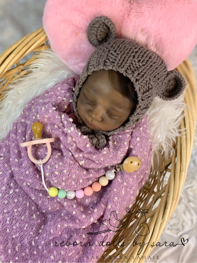 Black african american aa reborn baby girl doll Realborn Alexa Sleeping by Bountiful Baby wearing the brown Lovey hand knitted newborn baby bear hat with matching teddy.