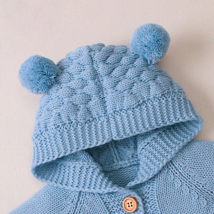 Close-up of the hood on a blue knitted bear romper for reborn dolls showing two pompoms that resemble bear ears.