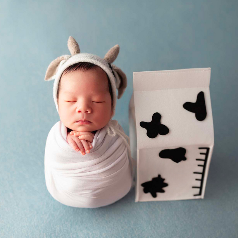 Newborn baby wearing black and white knitted crochet cow hat and matching cow stuffie for reborn dolls, newborn photography, reborn photoshoots, and cuddle babies.