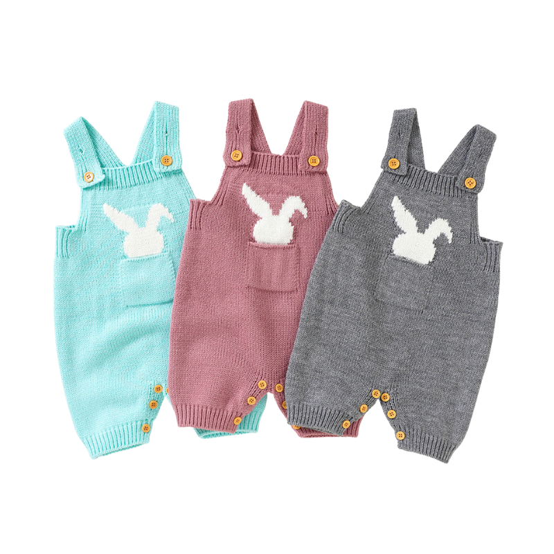 Three knitted overall shorts with front pockets on the chest and a little white silhouette of a bunny sticking out of the pocket. From left to right the colours are aqua blue, pink and grey and they are made for babies or reborn dolls.