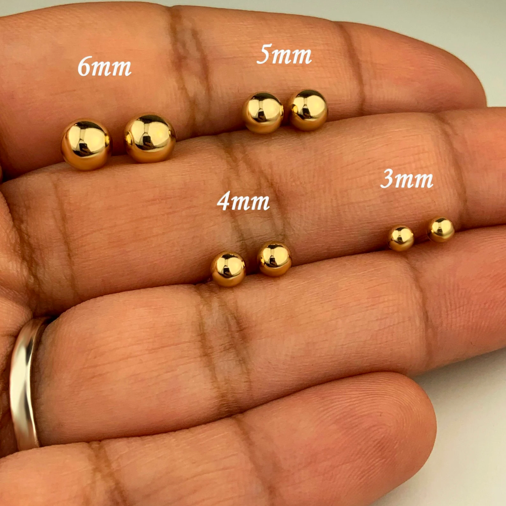 Black hand holding four pairs of yellow gold stud earrings to illustrate their respective sizes: 6mm, 5mm, 4mm and 3mm.  