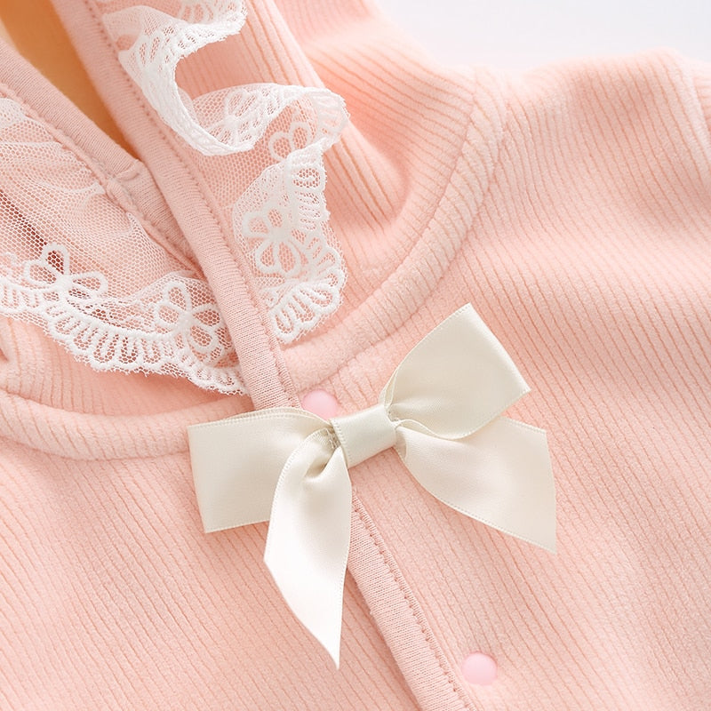 Close-up of the white silky bow on the neckline of a pink button-down baby snowsuit for reborn girl dolls with pixie hood, lace trim on the hood, and a white silky bow at the neckline.