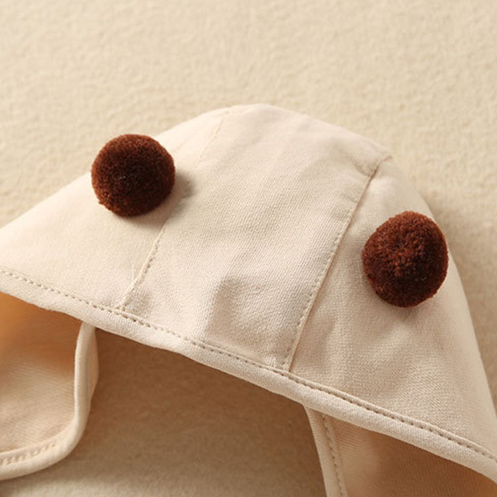 Close up of beige bonnet with two brown pompoms on the top.