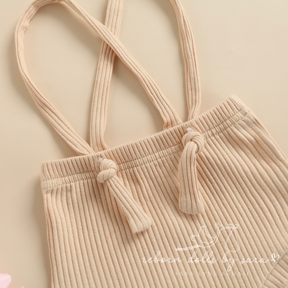 Close-up of the waist area and suspenders tied on a pair of beige ribbed boho baby bloomers with suspenders for reborn baby dolls.