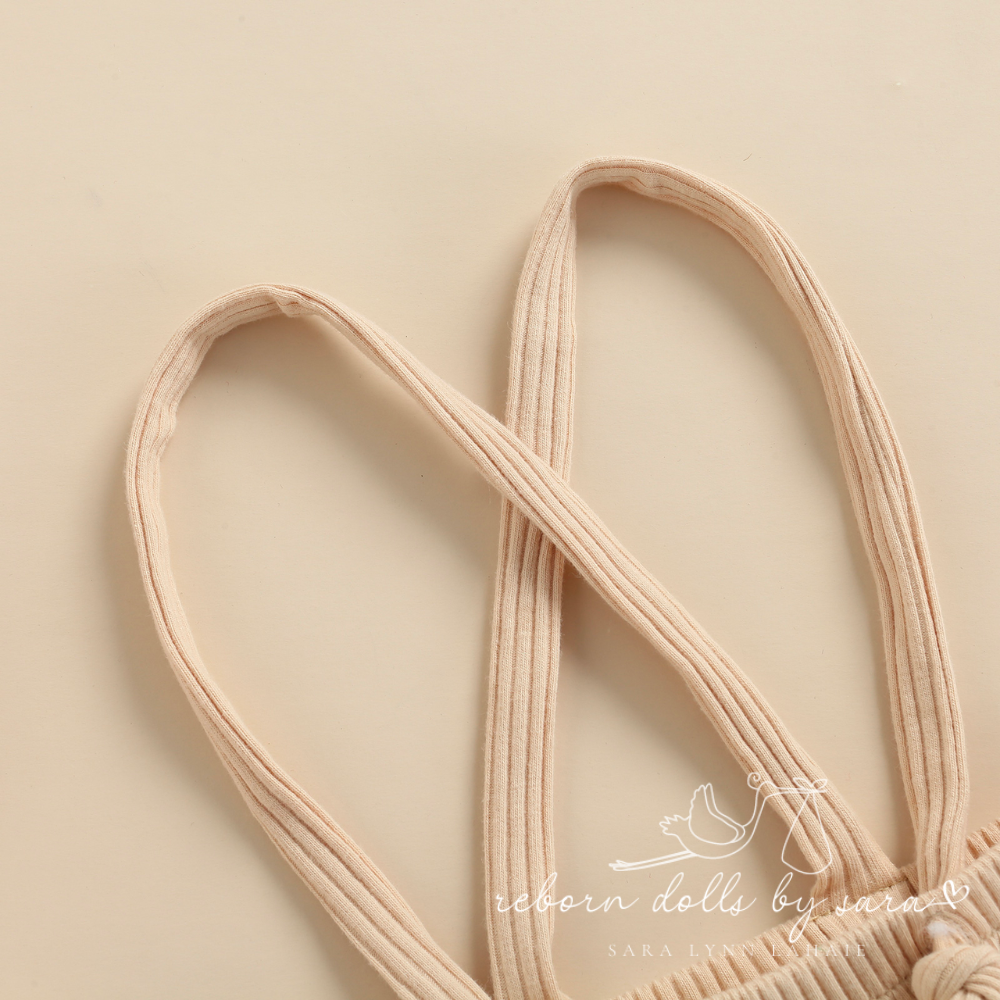 Close-up of suspenders on a pair of beige ribbed boho baby bloomers with suspenders for reborn baby dolls.
