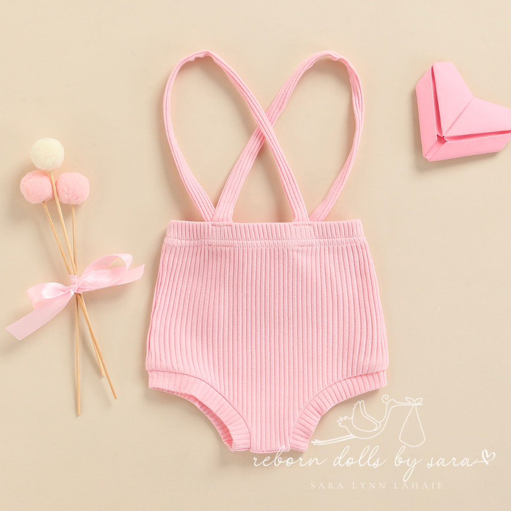 Back of a pair of baby pink ribbed boho baby bloomers with suspenders for reborn baby dolls.