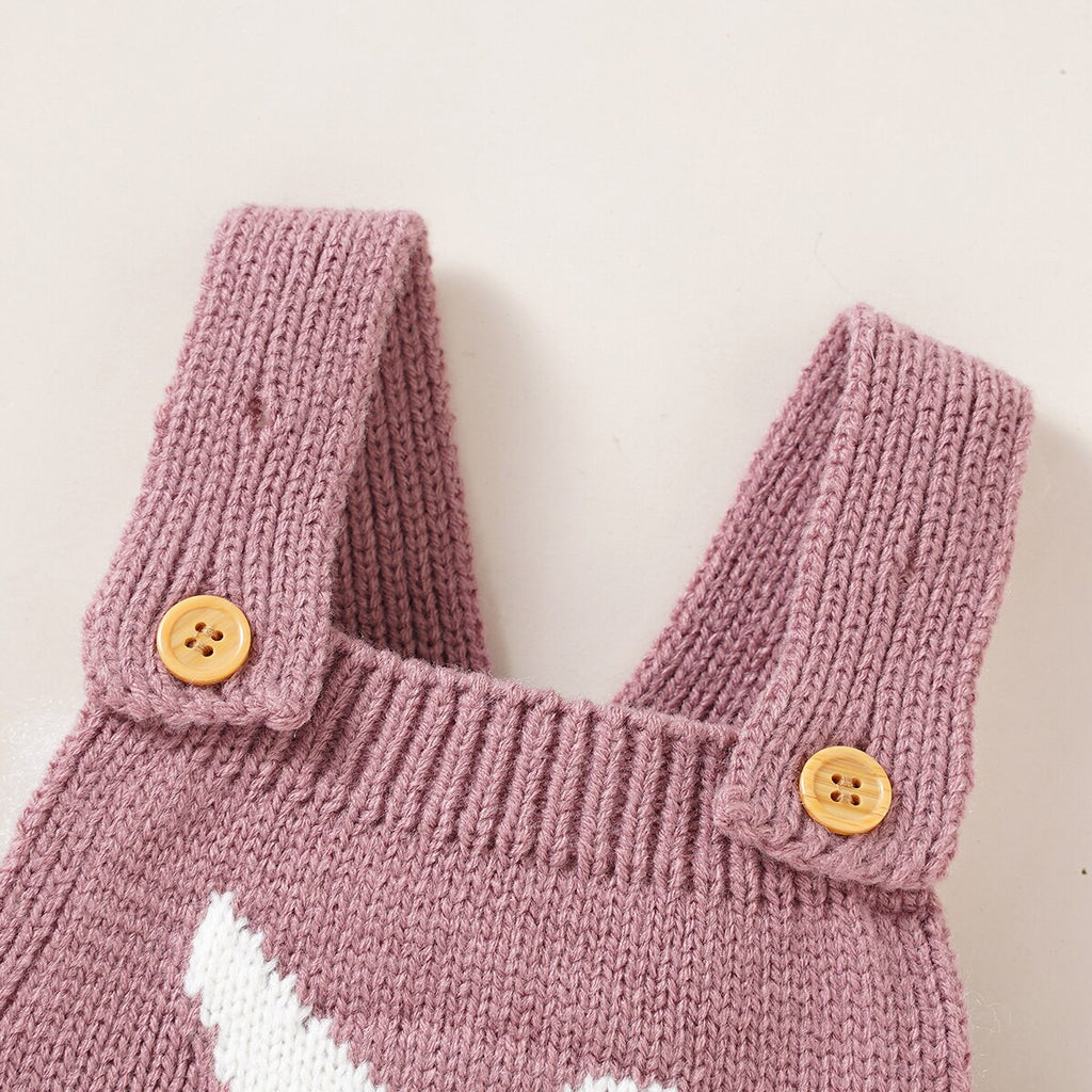 Close-up of the shoulder straps and top of the bib on a blush pink knitted overall romper with a rabbit on the chest for reborn dolls.