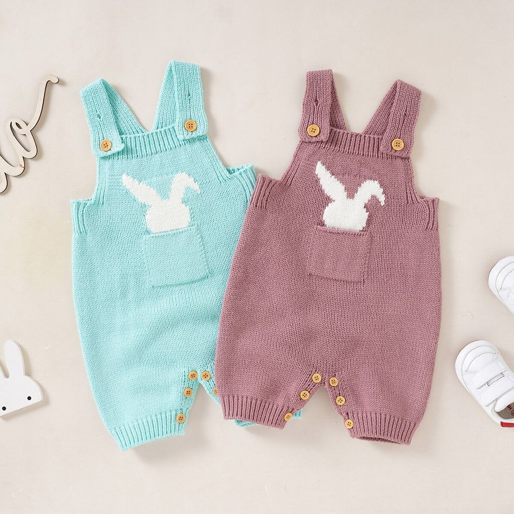 On the left an aqua blue knitted overall onesie with a white rabbit sticking out of the pocket for reborn dolls and on the right a pink version of the same romper for sale on the Reborn Dolls by Sara website and called You Make Me So Hoppy.