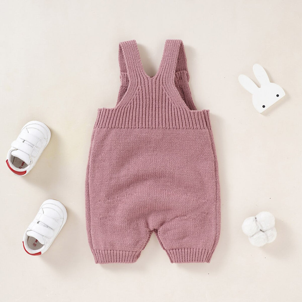 The back of a blush pink knitted overall romper with a pocket on the chest and a white rabbit coming out of the pocket for reborn dolls.