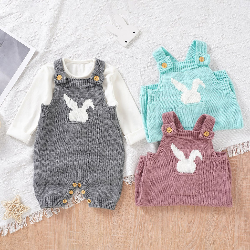 Three knitted overall shorts with front pockets on the chest and a little white silhouette of a bunny sticking out of the pocket. From left to right the colours are aqua blue, pink and grey and they are made for babies or reborn dolls.