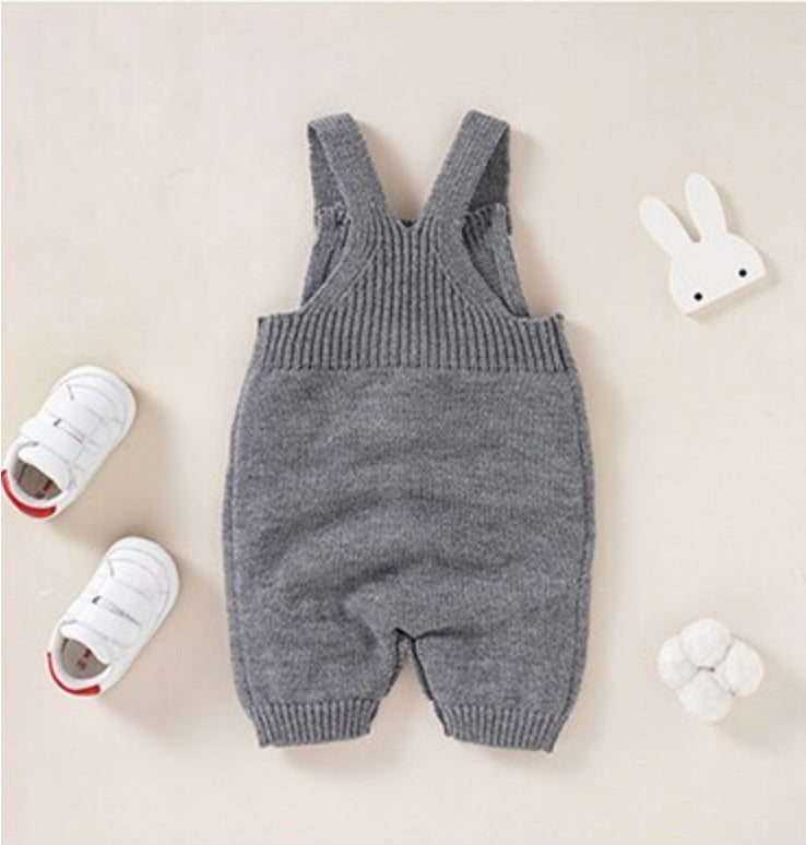 Back of grey knitted overall shorts for reborn dolls with a white silhouette of a bunny rabbit sticking out of the pocket.