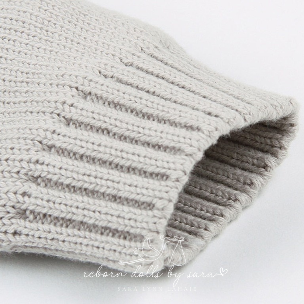 Close-up of the sleeve cuff on a grey knitted long-sleeve sweater onesie romper for reborn baby dolls.