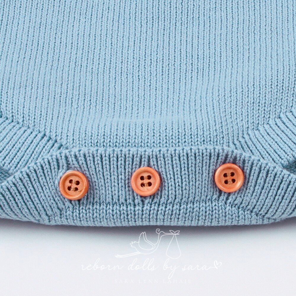Close-up of the buttons on the crotch of a blue long sleeve sweater onesie romper for reborn baby dolls.