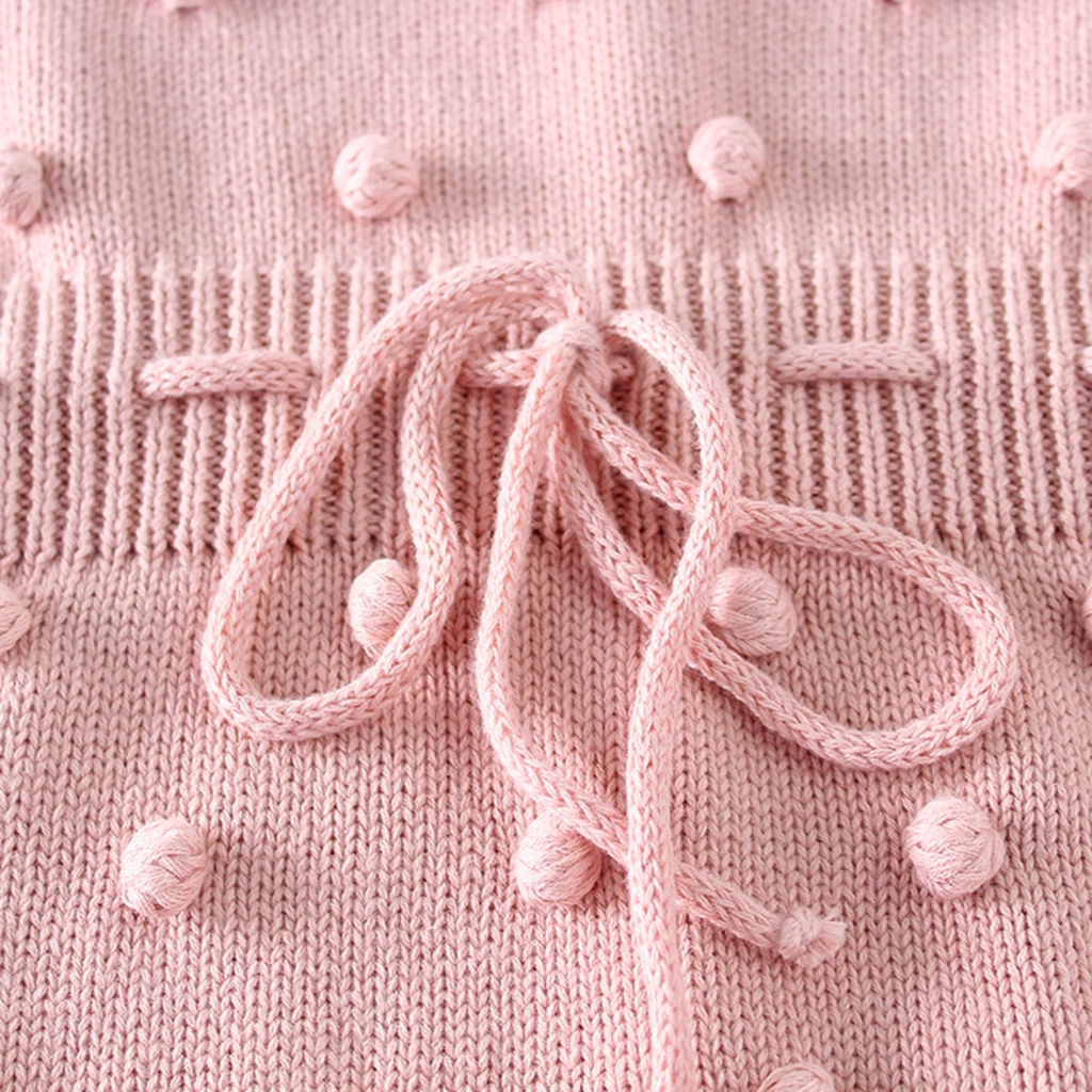 Close-up of the drawstring on the baby pink sleeveless knitted bubble romper with pink pompoms on the front, buttons on the shoulders, and buttons at the crotch. It also features a functional drawstring and is made to fit newborns baby girls to 2 year olds and reborn dolls.