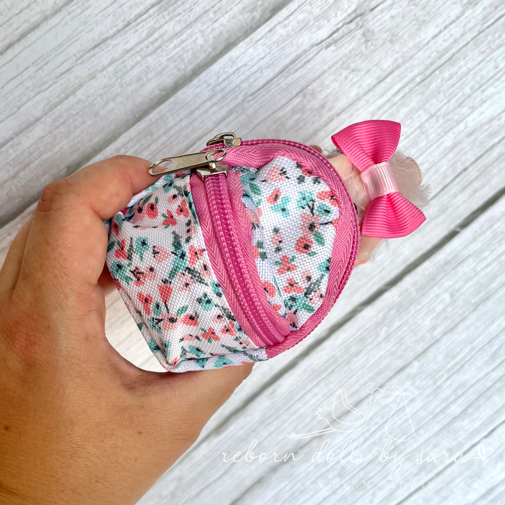 Me holding a silicone mini piglet who is wearing a pink and white floral miniature backpack.