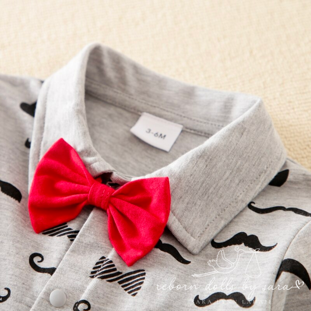 Grey long-sleeve button-up collared romper with black moustaches all over it and a red bow tie for newborn babies and reborn dolls.