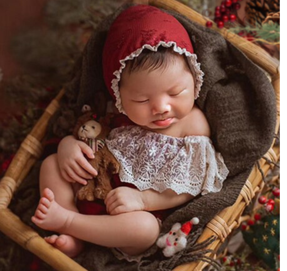 Real newborn baby girl in a newborn photoshoot holding a bear dressed in a reindeer costume. Reborn baby doll teddy bear toys that can be used by newborn photographers as well as newborn photography props.