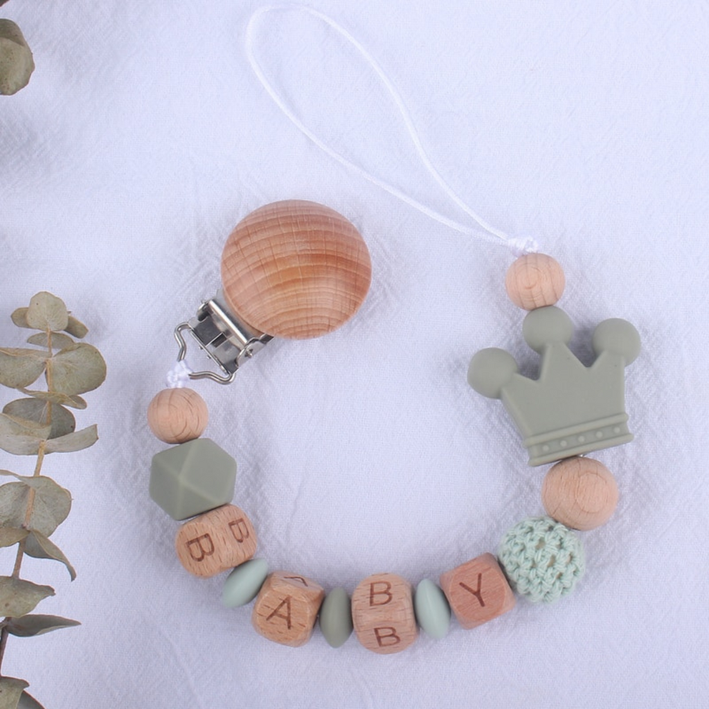 Sage and mint green personalized silicone pacifier clips with wooden fastener, crown bead, crochet beads, wooden beads with spacers between them, and silicone beads with baby's name for reborn baby dolls.