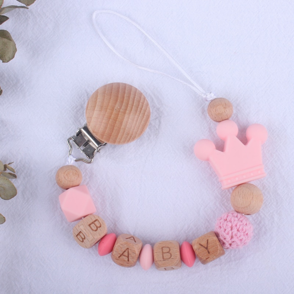 Baby pink and hot pink personalized silicone pacifier clips with wooden fastener, crown bead, crochet beads, wooden beads with spacers between them, and silicone beads with baby's name for reborn baby dolls.