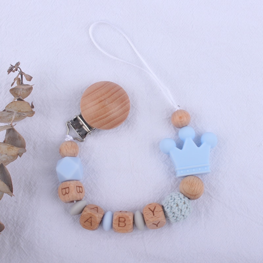 Light powder blue and light grey personalized silicone pacifier clips with wooden fastener, crown bead, crochet beads, wooden beads with spacers between them, and silicone beads with baby's name for reborn baby dolls.