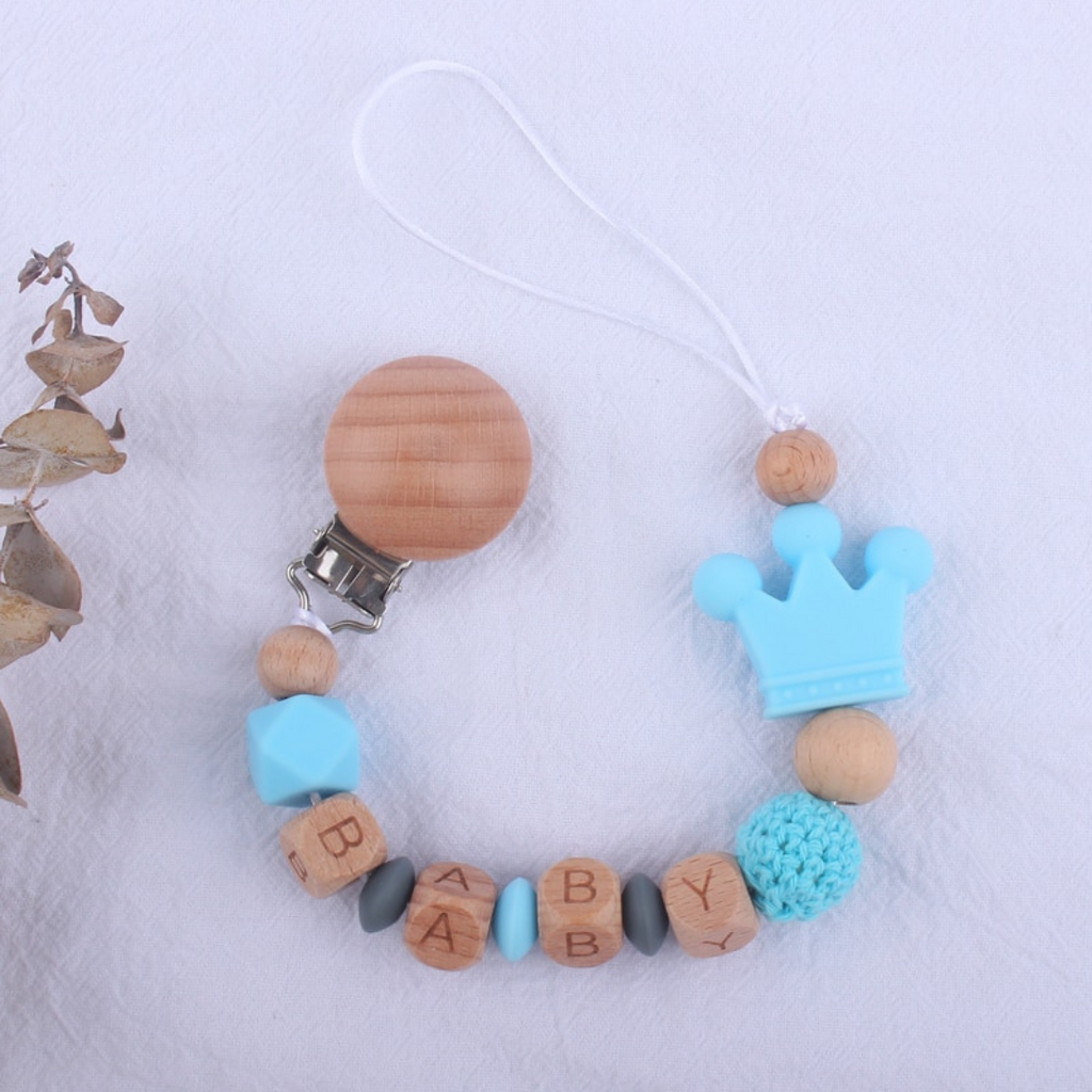 Cyan blue and dark grey personalized silicone pacifier clips with wooden fastener, crown bead, crochet beads, wooden beads with spacers between them, and silicone beads with baby's name for reborn baby dolls.