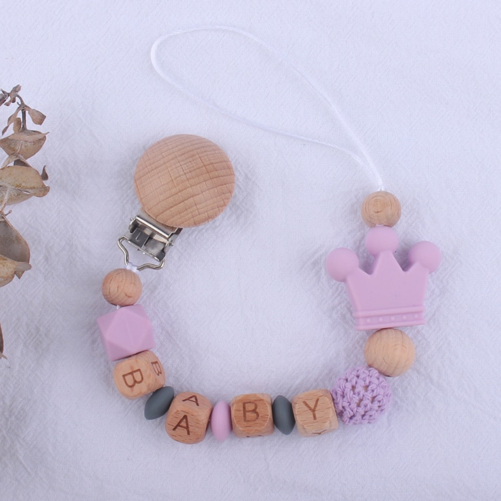 Lilac purple and dark grey personalized silicone pacifier clips with wooden fastener, crown bead, crochet beads, wooden beads with spacers between them, and silicone beads with baby's name for reborn baby dolls.