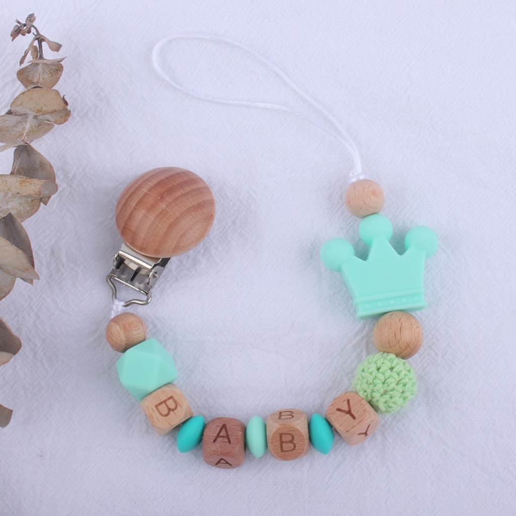 Mint green, turquoise and aqua blue personalized silicone pacifier clips with wooden fastener, crown bead, crochet beads, wooden beads with spacers between them, and silicone beads with baby's name for reborn baby dolls.