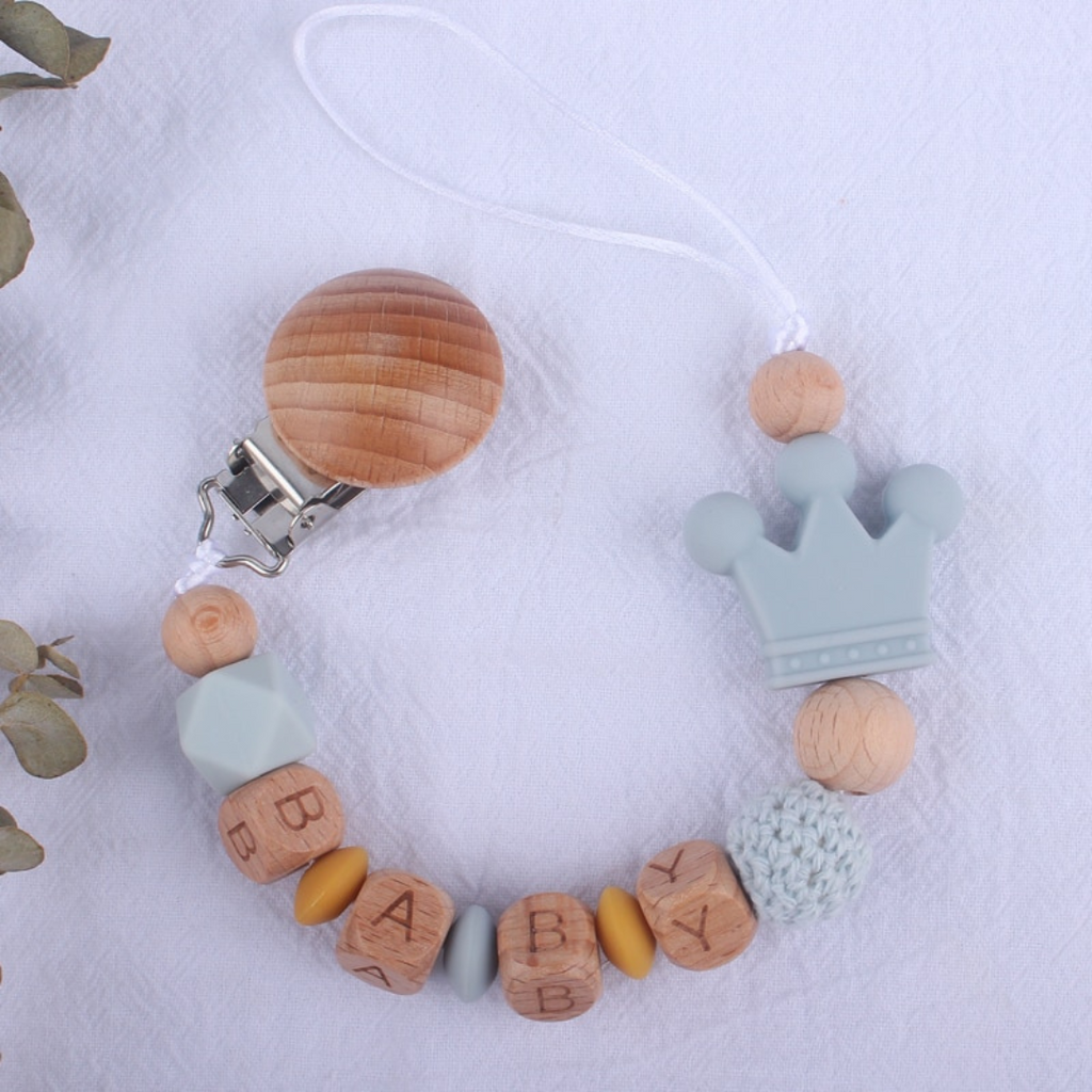 Powder blue aka light grey and mustard yellow personalized silicone pacifier clips with wooden fastener, crown bead, crochet beads, wooden beads with spacers between them, and silicone beads with baby's name for reborn baby dolls.