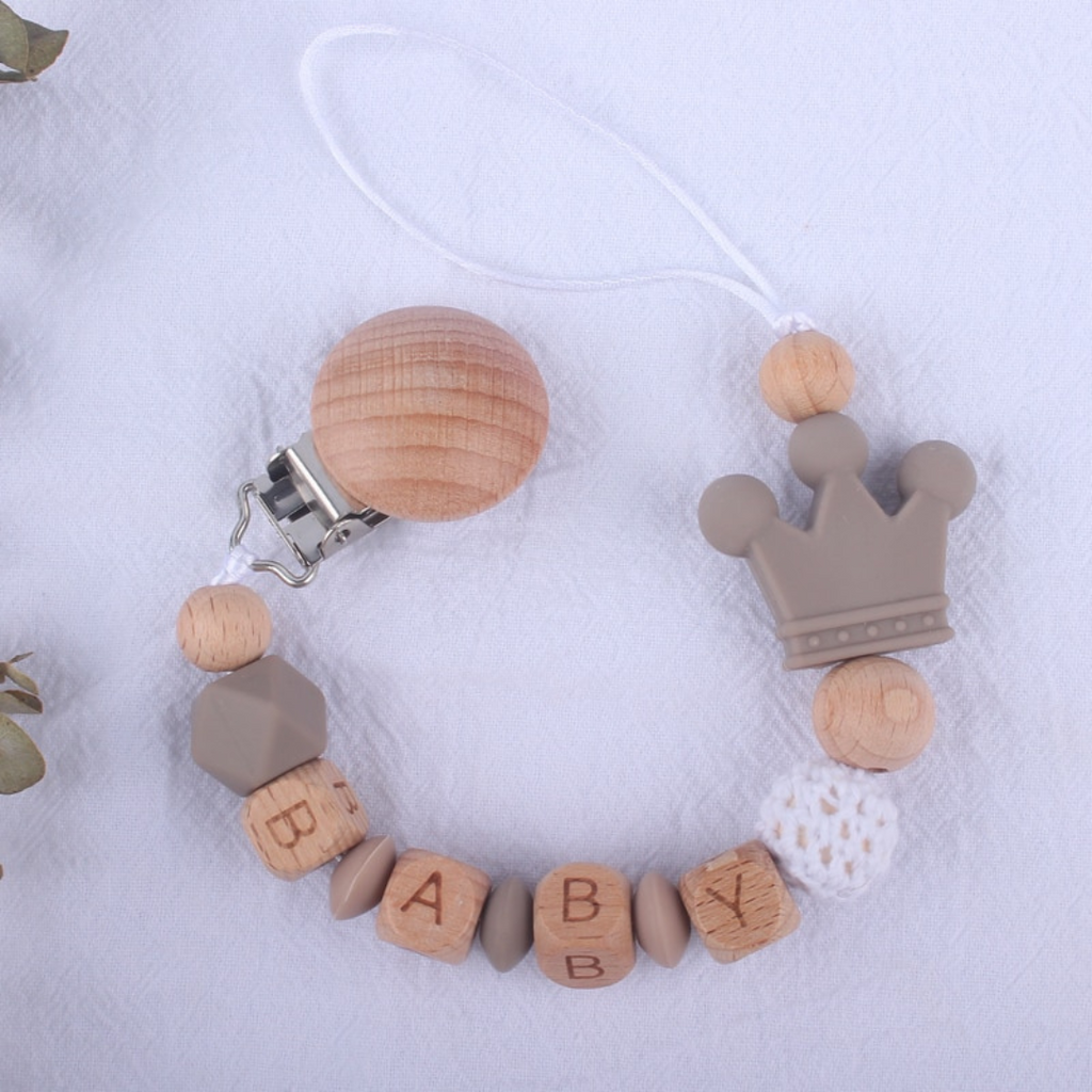 Taupe, beige and white personalized silicone pacifier clips with wooden fastener, crown bead, crochet beads, wooden beads with spacers between them, and silicone beads with baby's name for reborn baby dolls.