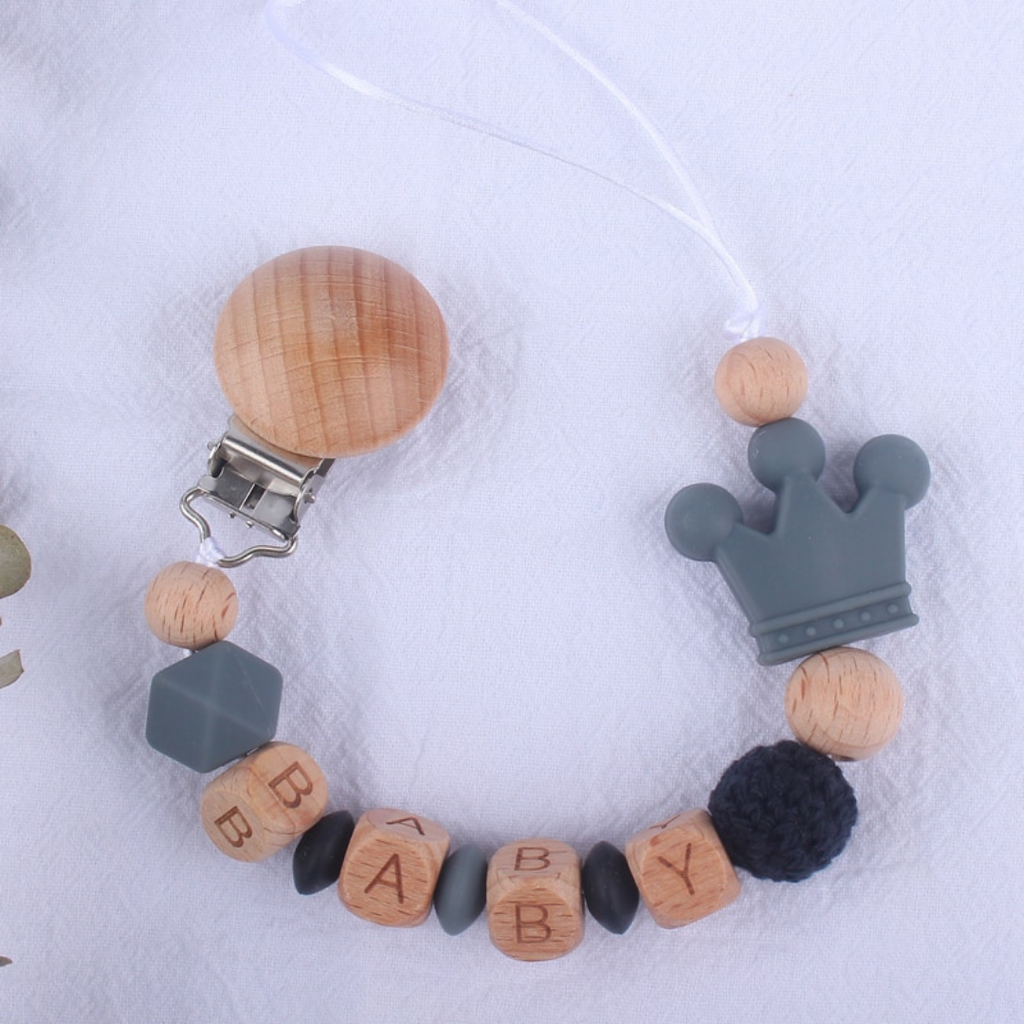 Dark grey and darker grey personalized silicone pacifier clips with wooden fastener, crown bead, crochet beads, wooden beads with spacers between them, and silicone beads with baby's name for reborn baby dolls.