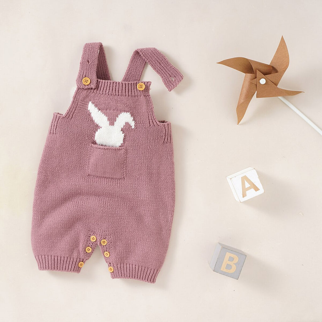 Blush pink knitted overall shorts for reborn dolls with a white silhouette of a bunny rabbit sticking out of the pocket.