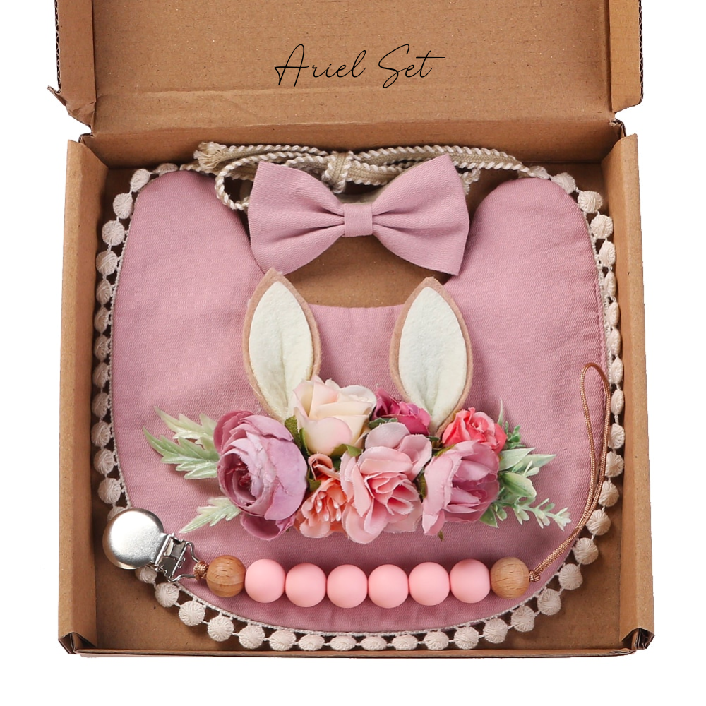 Deer ear floral newborn headband, pink bow headband, boho bib, and silicone pacifier cilp in a reborn baby girl doll box opening.