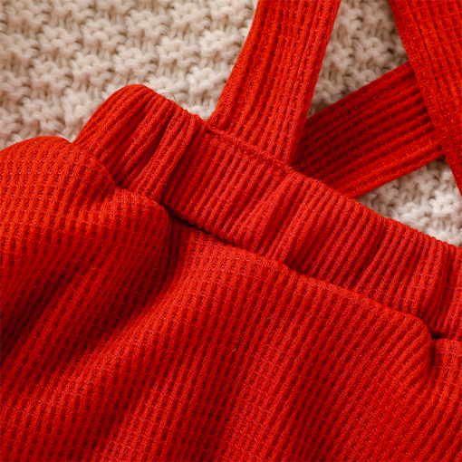 Close-up of the scarlet red dress that comes with a white long-sleeve onesie with white frills at the sleeve and orange and yellow floral pattern, with green leaves and red berries. Comes with a scarlet red waffle knit dress with straps that button on the inside of the dress and a matching nylon bow headband for reborn baby girls.