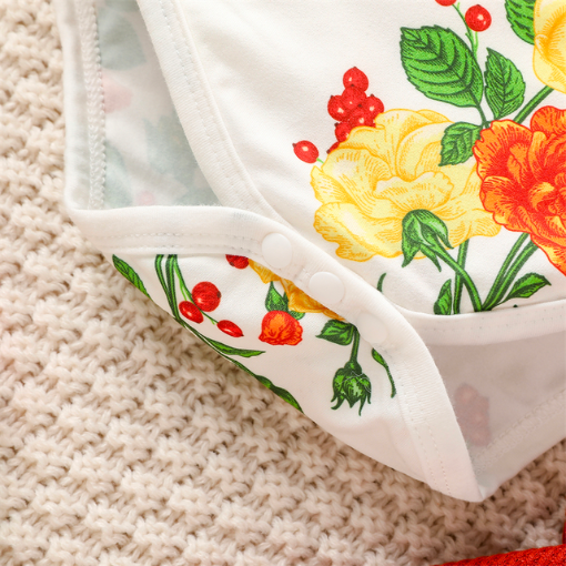 Close-up of the crotch and three snap button closure on a white long-sleeve onesie with white frills at the sleeve and orange and yellow floral pattern, with green leaves and red berries. Comes with a scarlet red waffle knit dress with straps that button on the inside of the dress and a matching nylon bow headband for reborn baby girls.