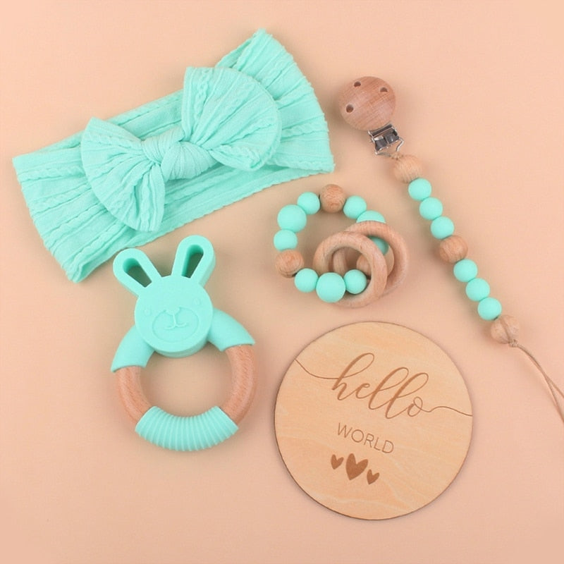 Aqua Turquoise Five Piece Boho Baby Girl Gift Set and reborn doll box opening with teething ring, headband, milestone card that says hello world, silicone pacifier clip and silicone teething bracelet with wooden rings.