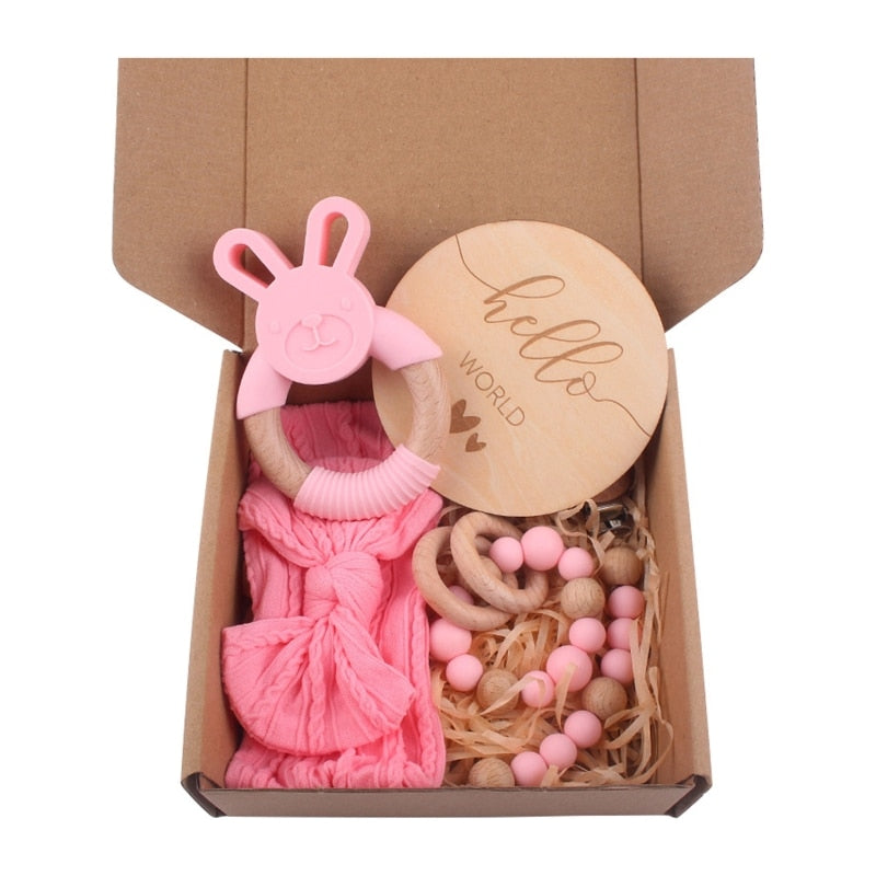 Pink Five Piece Boho Baby Girl Gift Set and reborn doll box opening with teething ring, headband, milestone card that says hello world, silicone pacifier clip and silicone teething bracelet with wooden rings.