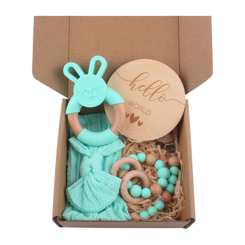 Aqua turquoise Five Piece Boho Baby Girl Gift Set and reborn doll box opening with teething ring, headband, milestone card that says hello world, silicone pacifier clip and silicone teething bracelet with wooden rings.