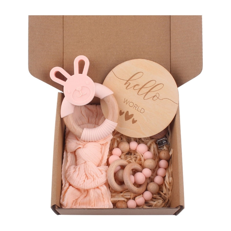 peachy pink Five Piece Boho Baby Girl Gift Set and reborn doll box opening with teething ring, headband, milestone card that says hello world, silicone pacifier clip and silicone teething bracelet with wooden rings.