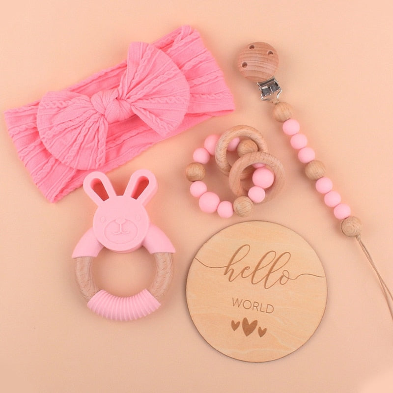 Pink Five Piece Boho Baby Girl Gift Set and reborn doll box opening with teething ring, headband, milestone card that says hello world, silicone pacifier clip and silicone teething bracelet with wooden rings.