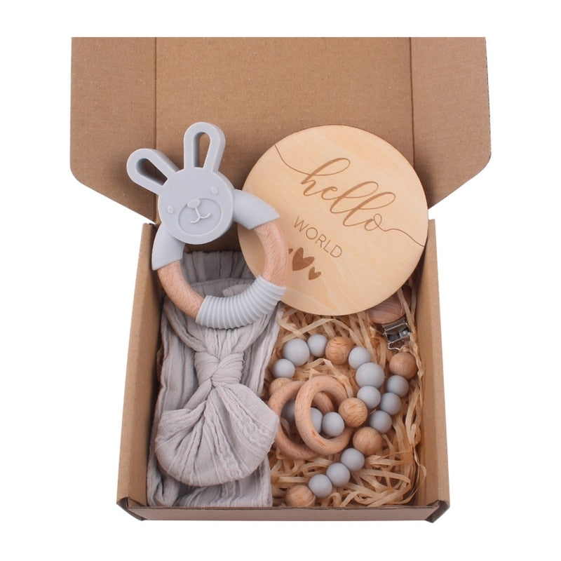 Grey Five Piece Boho Baby Girl Gift Set and reborn doll box opening with teething ring, headband, milestone card that says hello world, silicone pacifier clip and silicone teething bracelet with wooden rings.