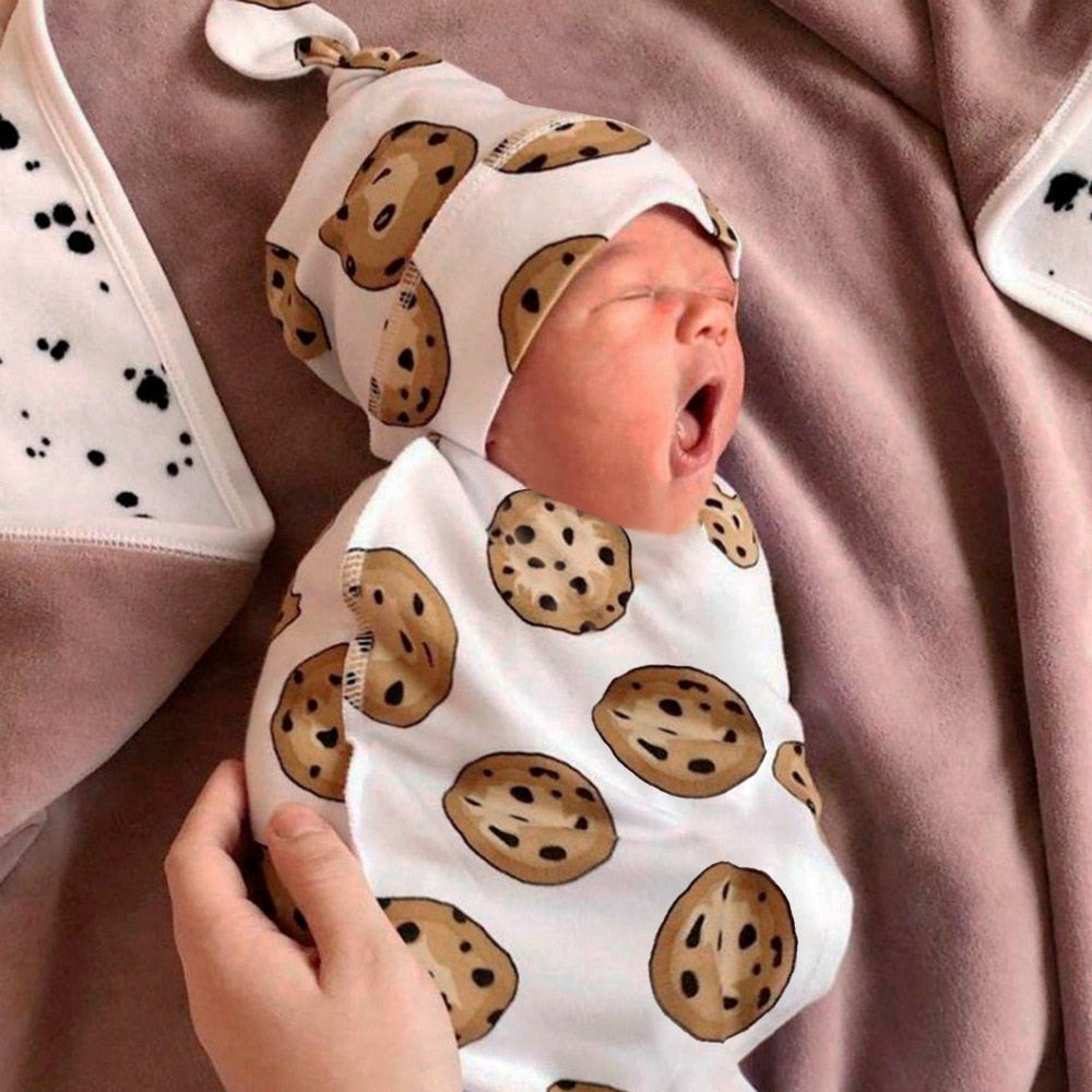 Newborn wearing a white sleep sack cocoon with cookies on it with a matching knotted baby hat for reborn dolls and cuddle babies.