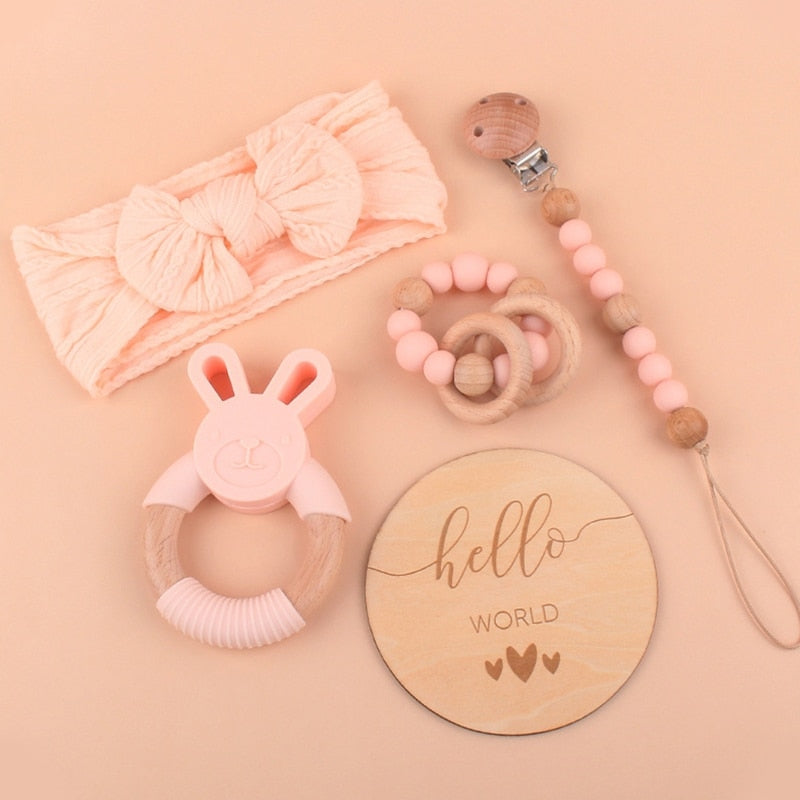 Peachy Pink Five Piece Boho Baby Girl Gift Set and reborn doll box opening with teething ring, headband, milestone card that says hello world, silicone pacifier clip and silicone teething bracelet with wooden rings.