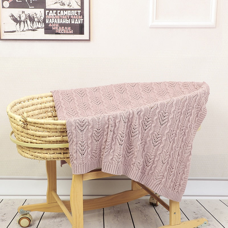 Blush pink coloured Fern Gully knitted baby blanket for reborn dolls and newborn babies over a bassinet.