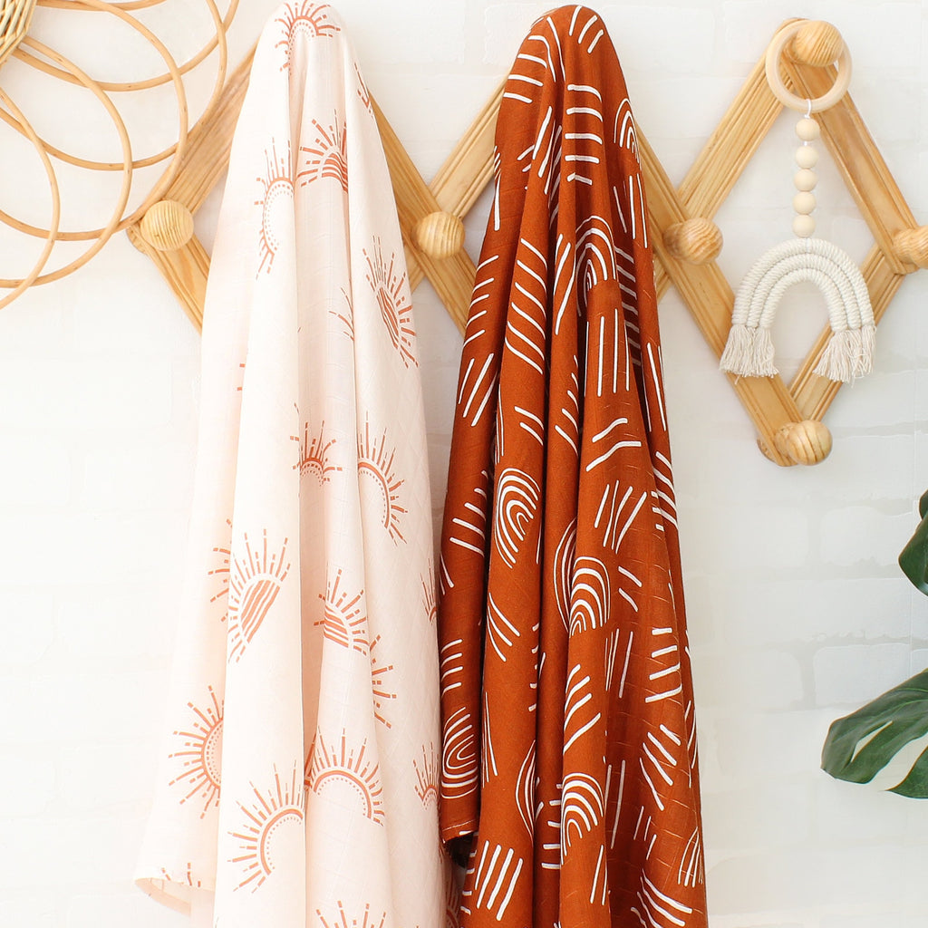 Two piece boho muslin swaddle blankets.  One is cream with boho suns on it and the other is rusty ginger orange with white rainbows for reborn dolls, newborn babies and photography.